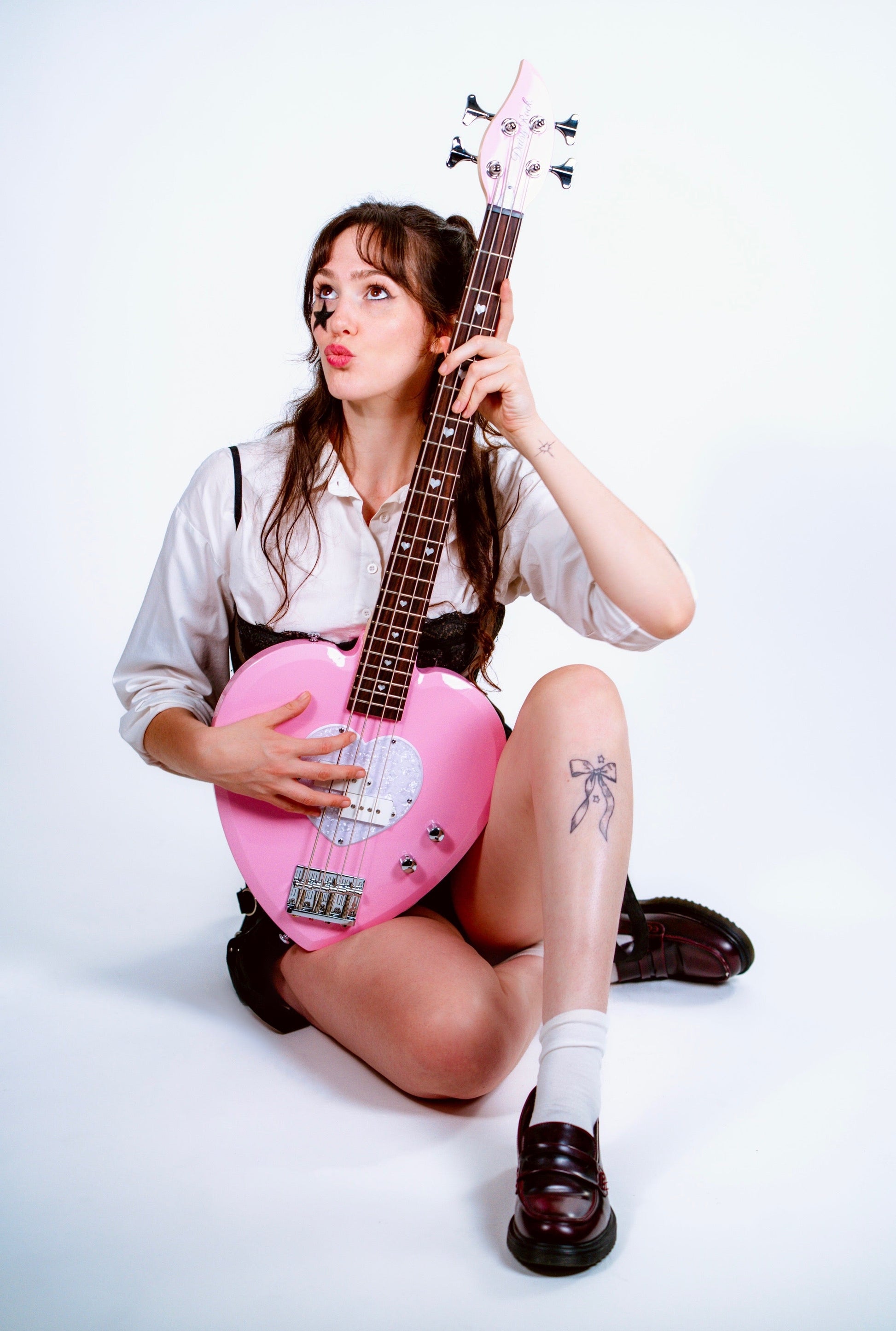 Person holding a pink heart-shaped bass guitar on a white background