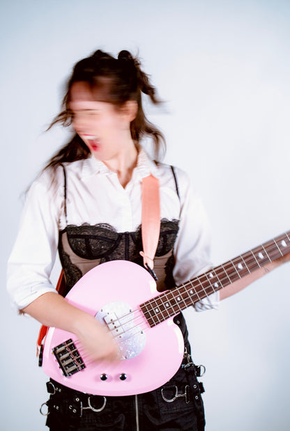 Person playing a pink electric bass guitar against a white background