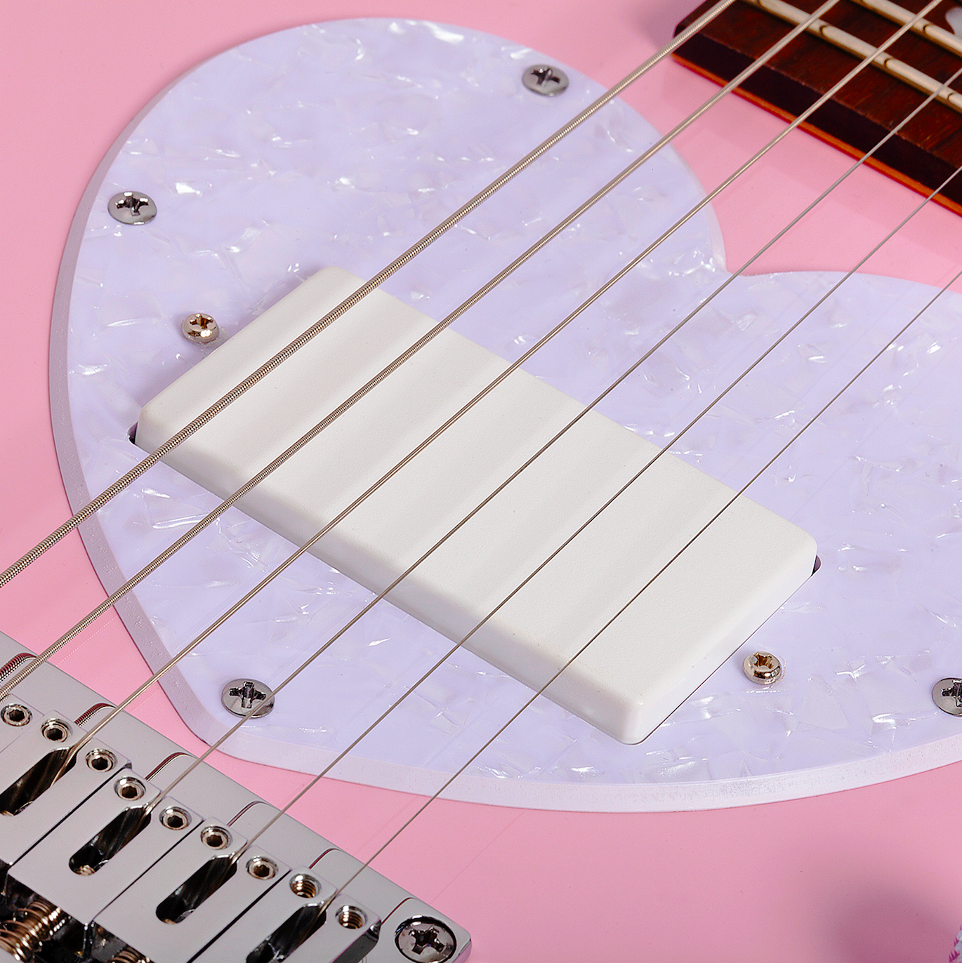 Close-up of a short scale pink electric guitar bridge and strings with a white pearlescent pick guard
