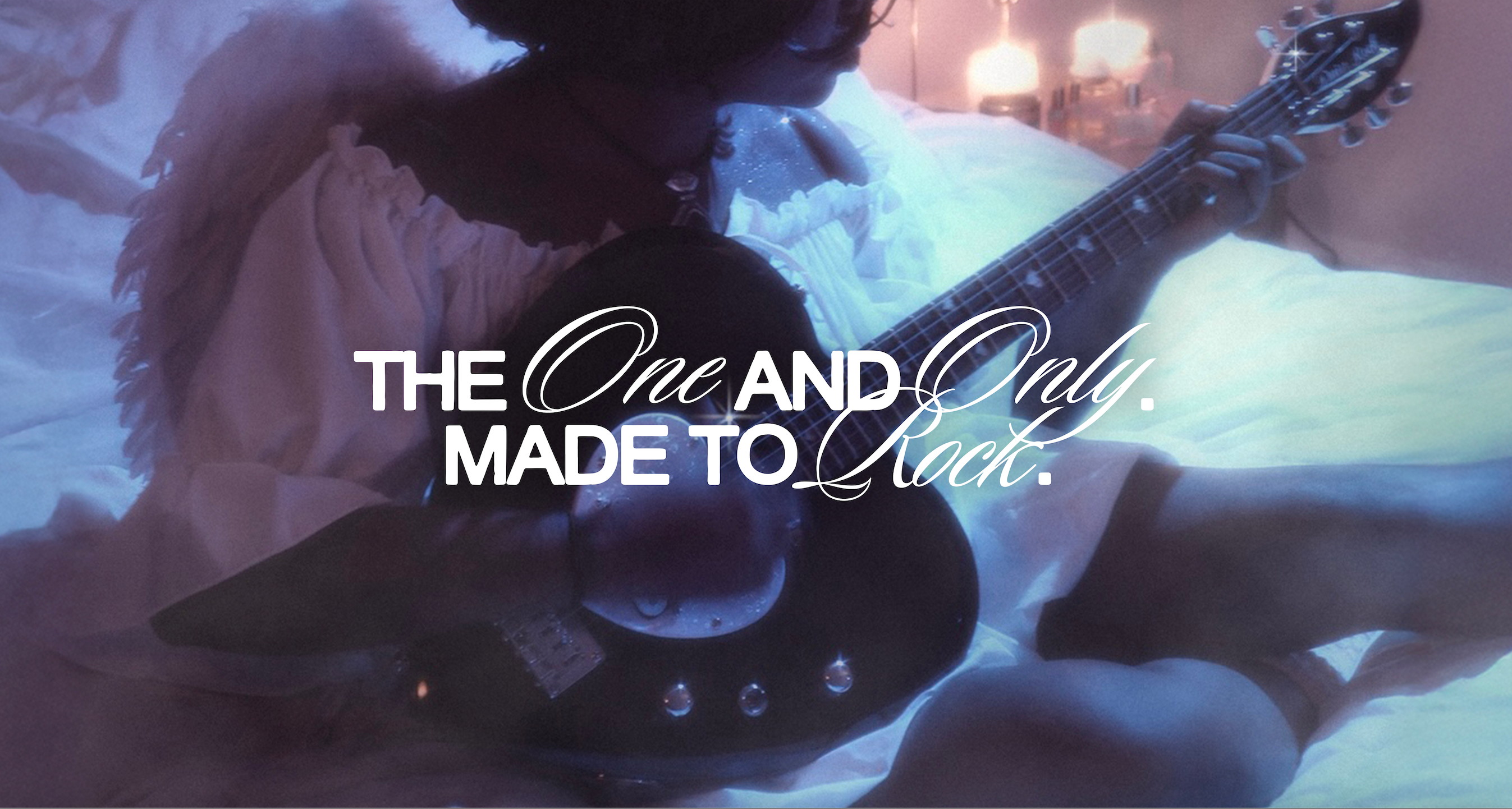 Model dressed as an angel playing a black, heart-shaped electric guitar in a dreamy room with purple and blue lighting