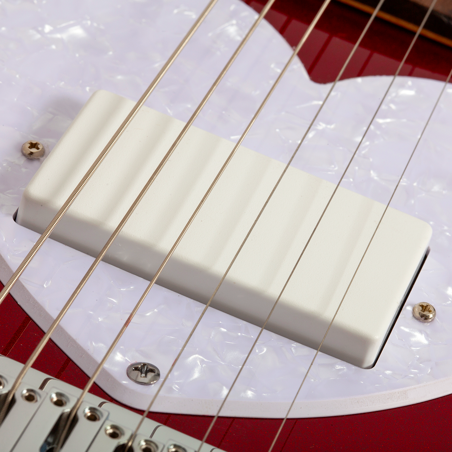Ultra close-up of a short scale red electric guitar bridge and strings with a white pearlescent pick guard