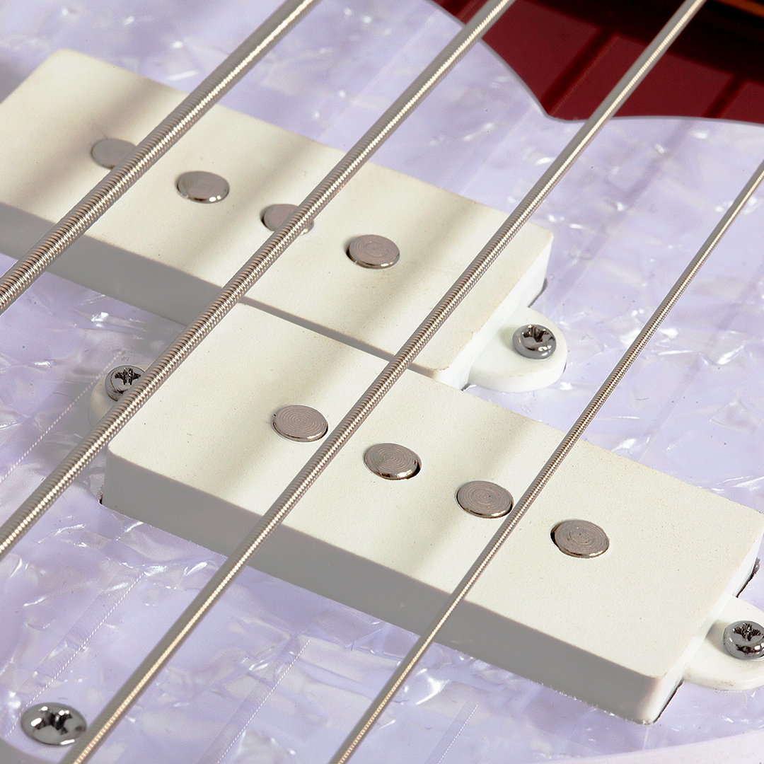 Ultra close-up of a red electric bass guitar bridge and strings with a white pearlescent pick guard